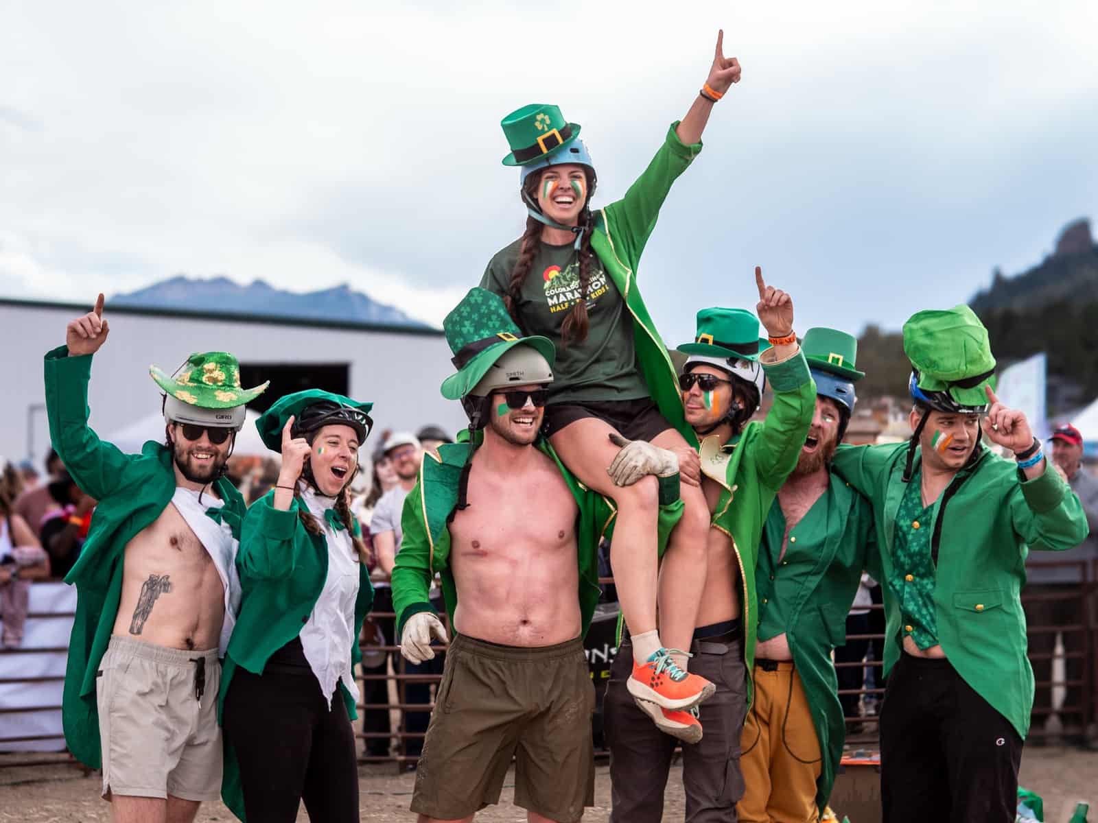 A leprechaun-costumed team celebrates, one teammate lifted onto shoulders with arms raised.