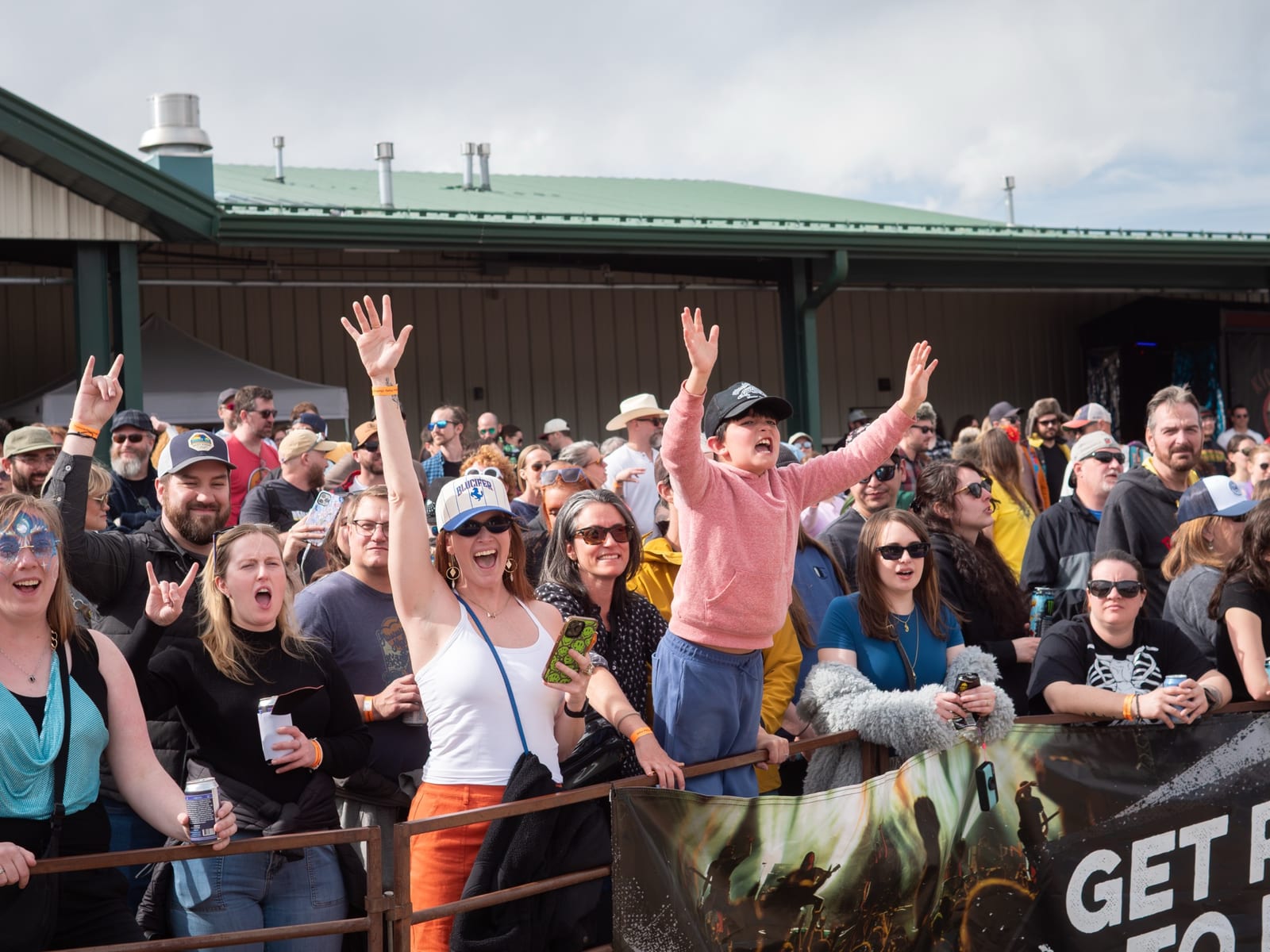 A young fan in a pink hoodie cheers with both arms up at the course fence.