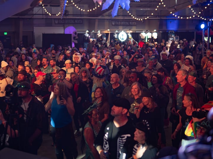 A packed indoor crowd dances under string lights at a night concert.