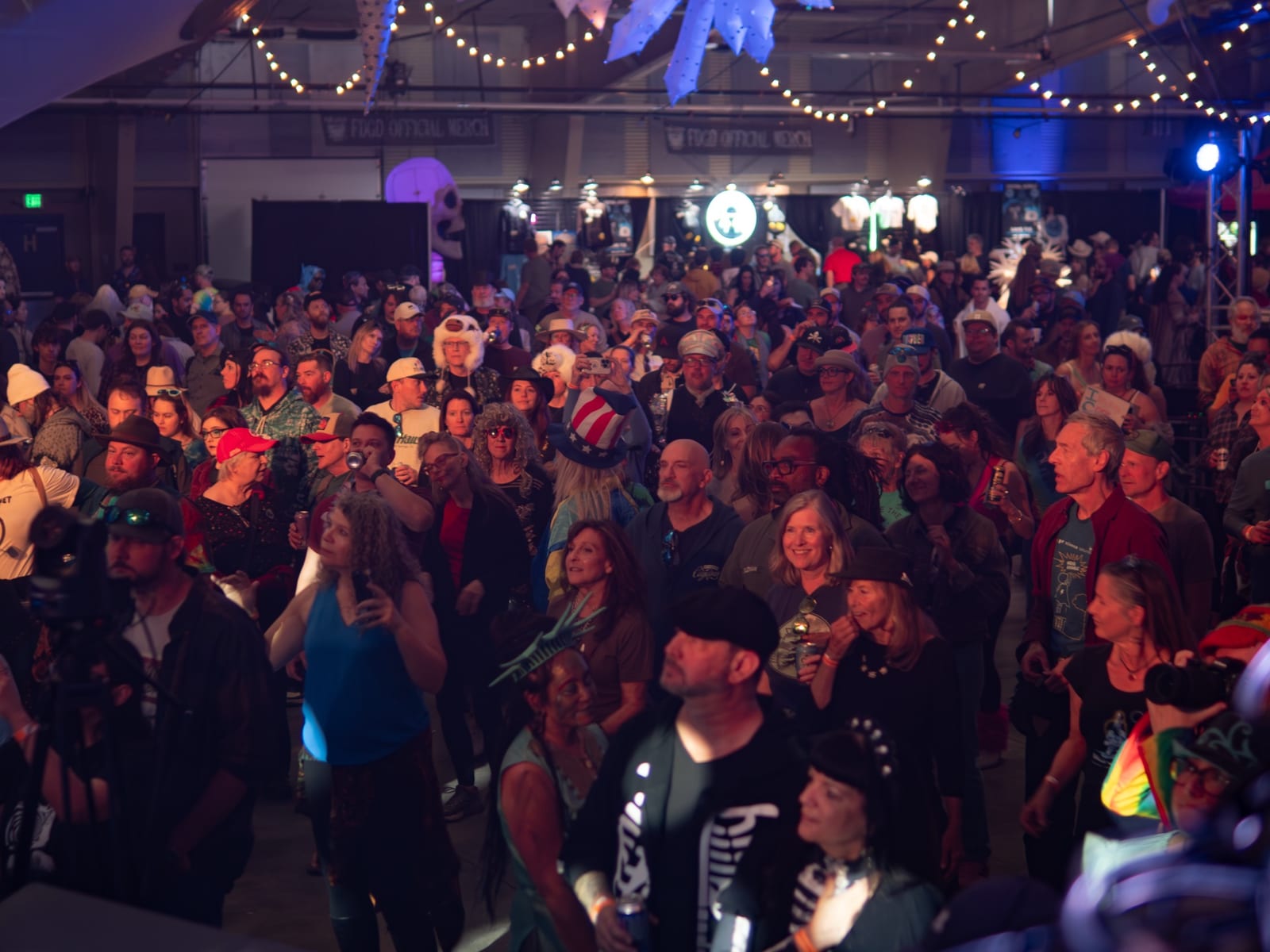 A packed indoor crowd dances under string lights at a night concert.