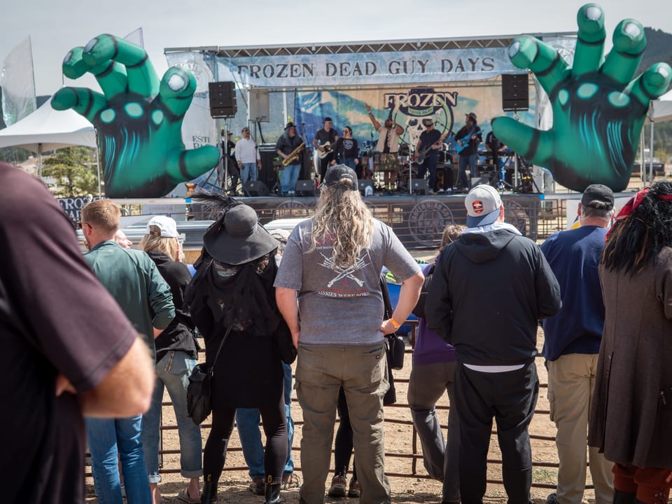 A band plays the outdoor stage between two giant green zombie hands as the crowd watches.