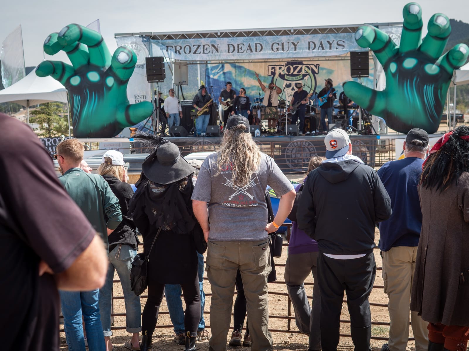 A band plays the outdoor stage between two giant green zombie hands as the crowd watches.