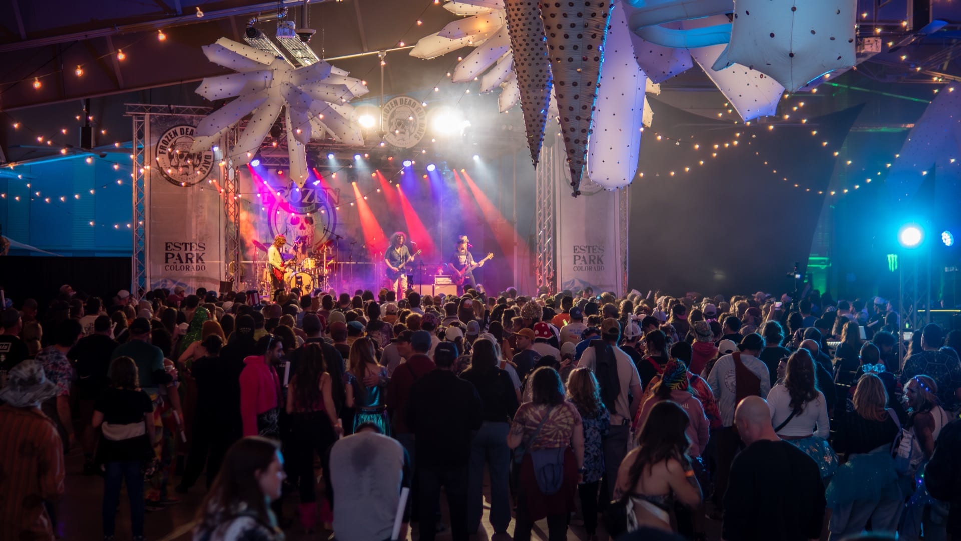 A band performs under red and blue lights to a packed indoor crowd.