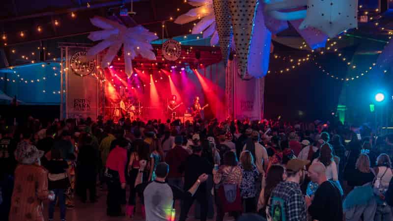A packed indoor concert under red stage lights and hanging snowflake decorations.