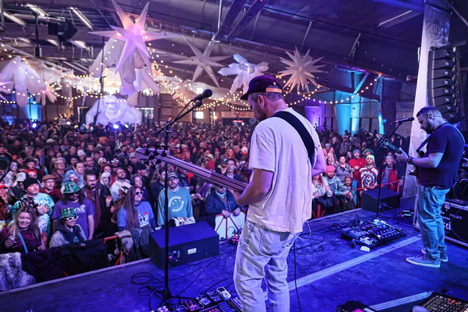 A guitarist plays to a crowd from an indoor stage washed in blue light.