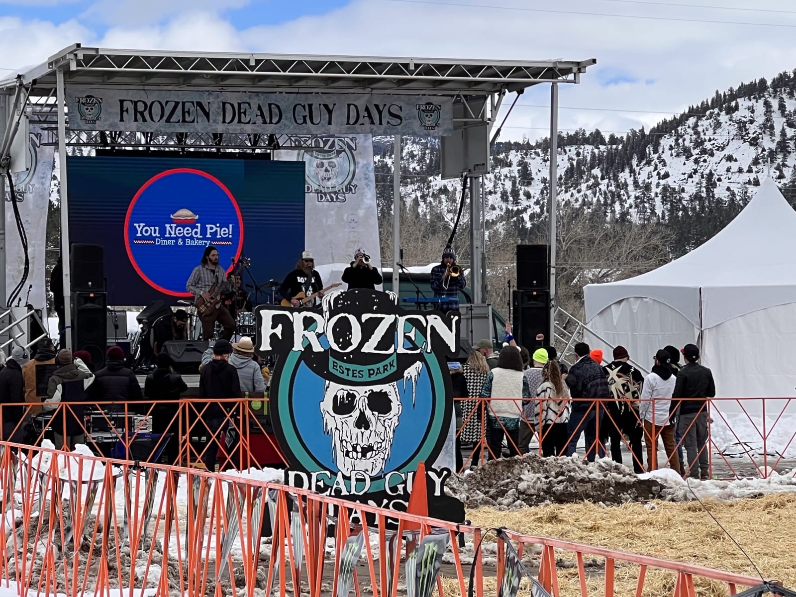 An outdoor stage with a giant skull-badge banner, snow on the ground and mountains behind.