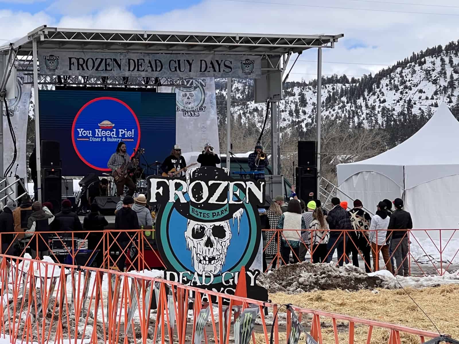 An outdoor stage with a giant skull-badge banner, snow on the ground and mountains behind.