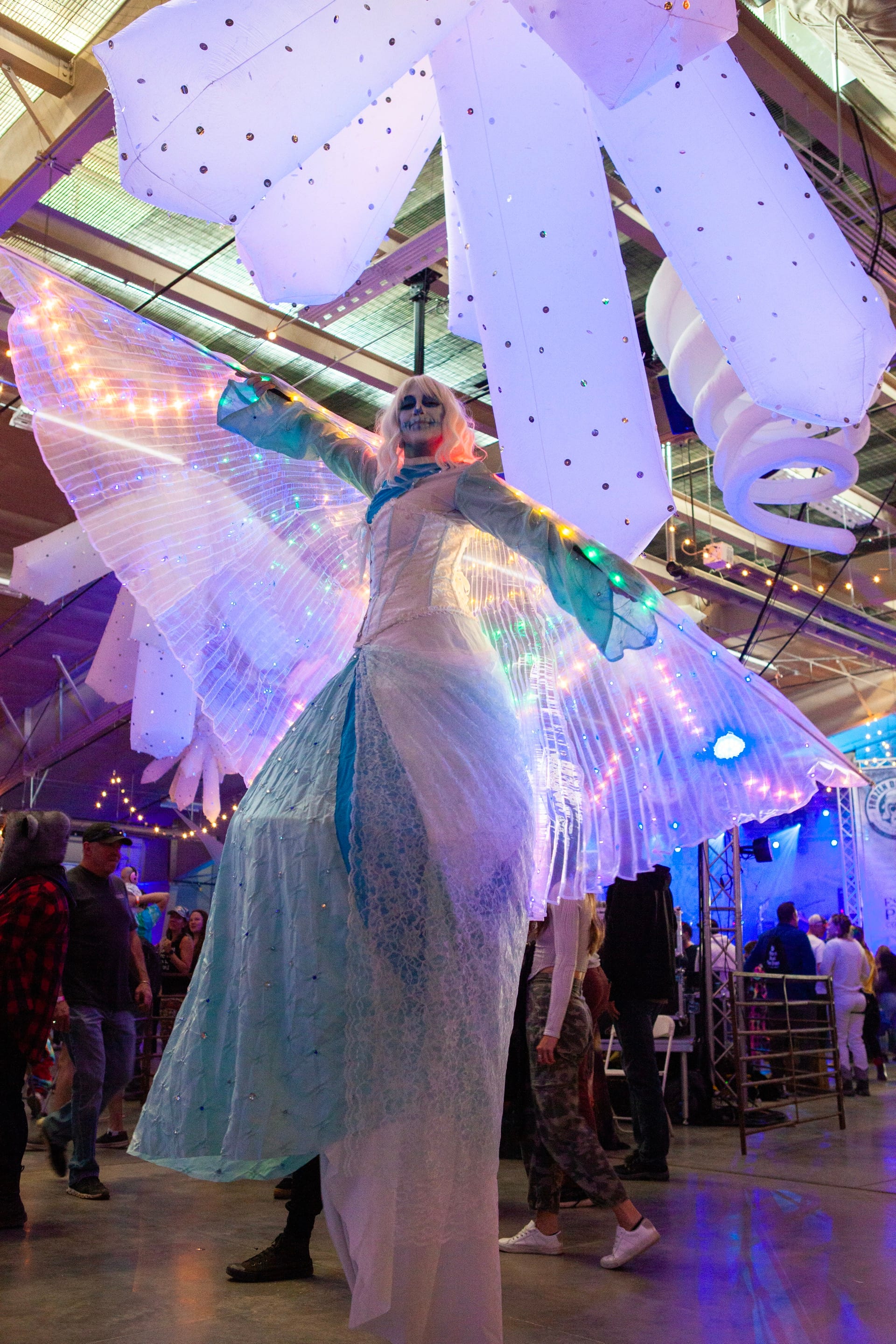 A performer on stilts in a flowing ice-queen costume towers over the indoor crowd.