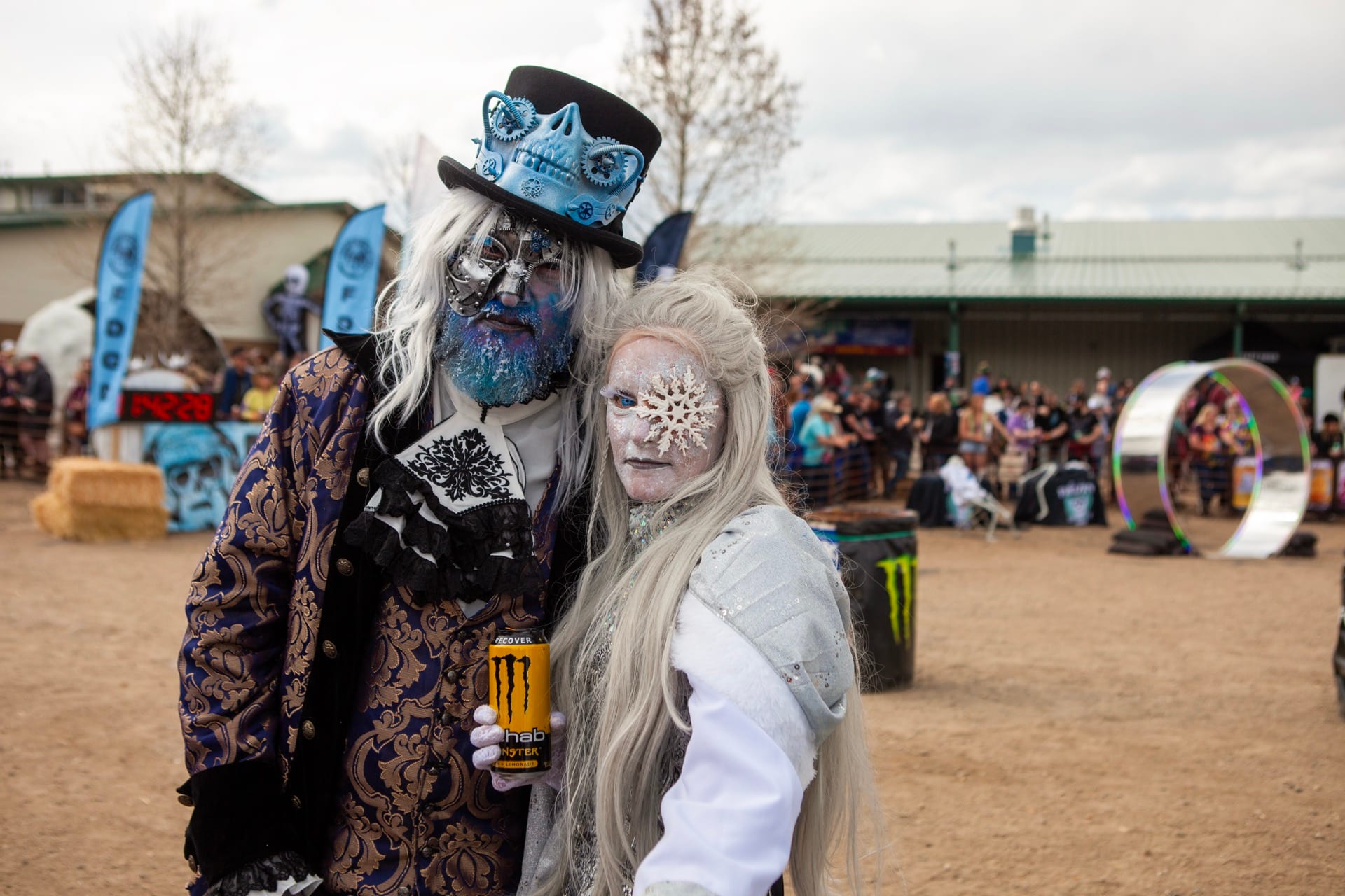 A costumed couple with blue skull face paint and white wigs pose on the festival grounds.