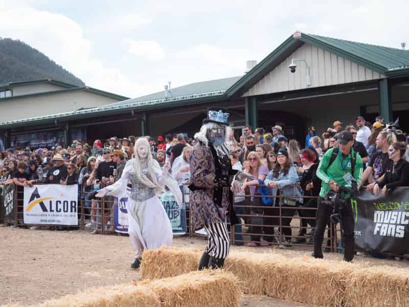 Costumed performers in white and black stroll past the crowd along the course fence.