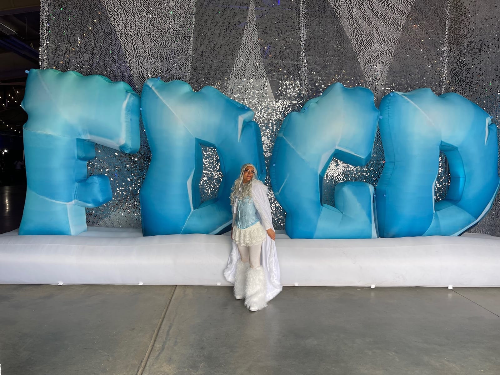 A festival-goer in white poses in front of giant inflatable ice-blue "FDGD" letters.