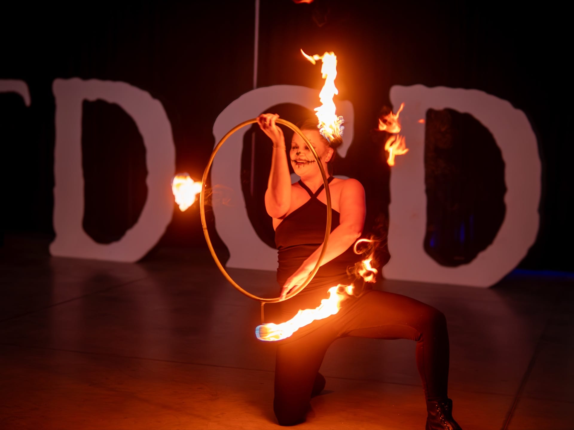 A fire performer spins a flaming hoop in front of illuminated FDGD letters.
