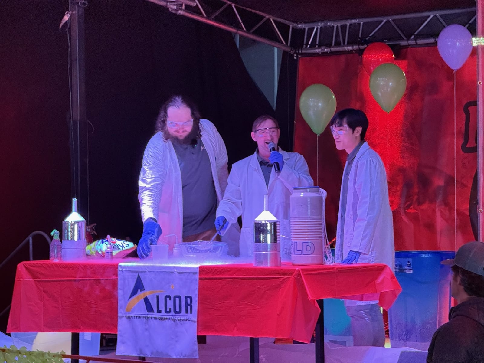 Scientists in lab coats run a liquid-nitrogen demonstration at the Alcor table.