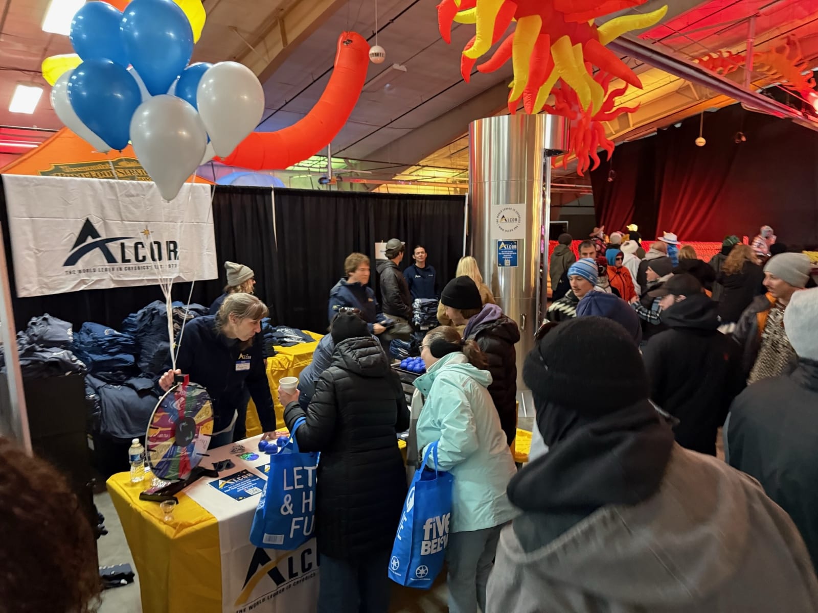 Festival-goers crowd the Alcor booth under balloons.
