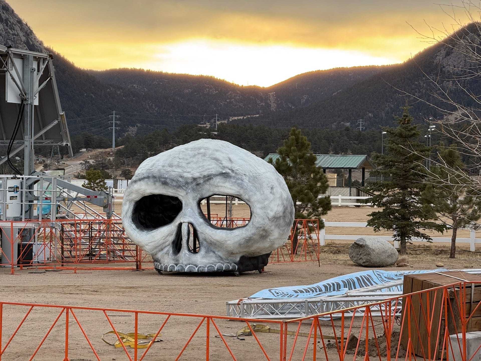 A giant skull sculpture on the festival grounds at sunset, mountains silhouetted behind.
