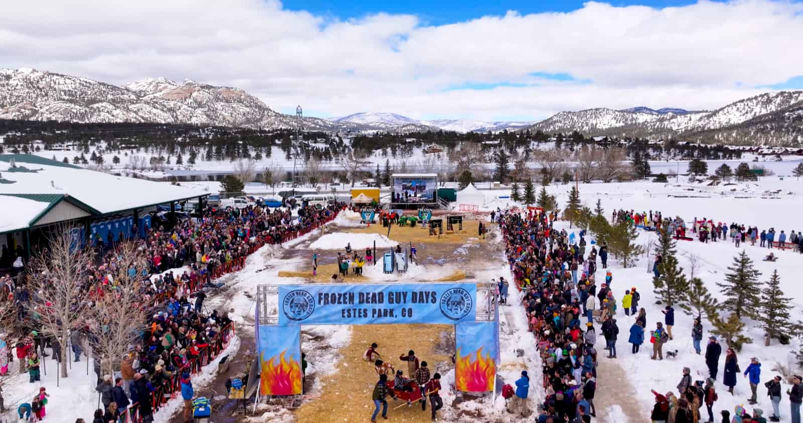 Aerial view of a snowy coffin course and crowd beneath the Frozen Dead Guy Days arch.