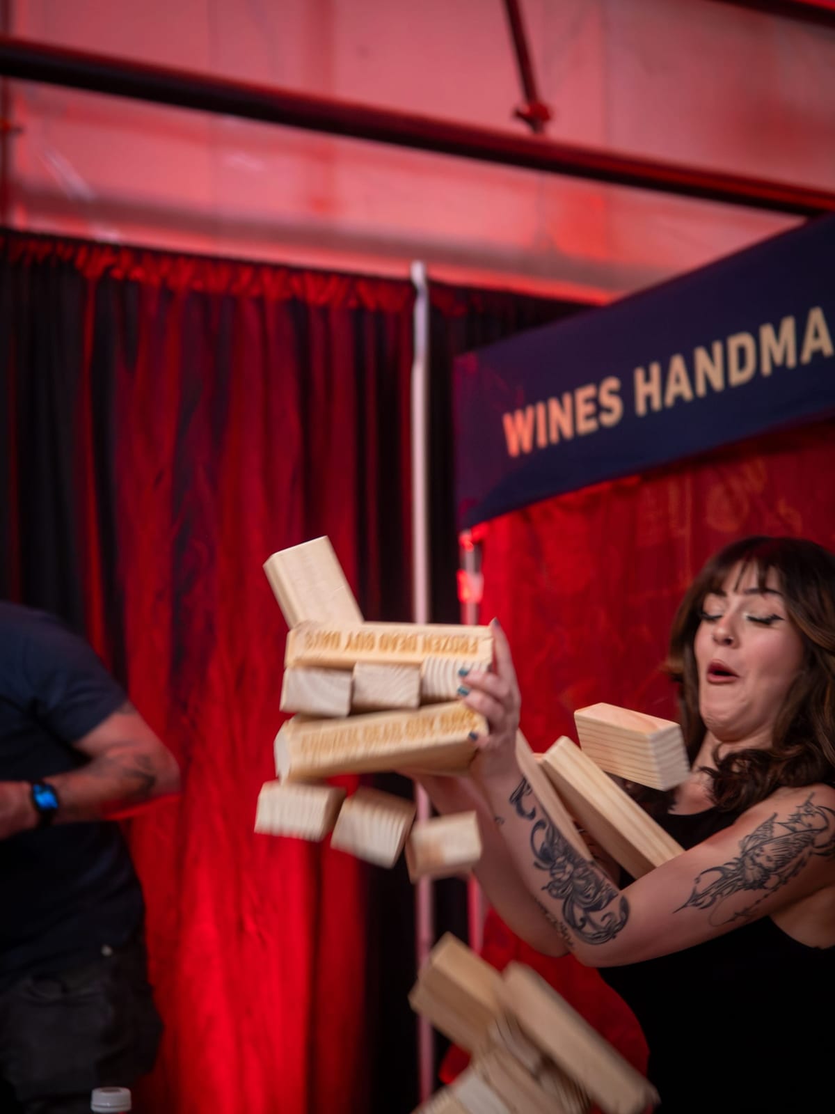 A giant wooden Jenga tower collapses mid-air as a woman flinches in surprise.