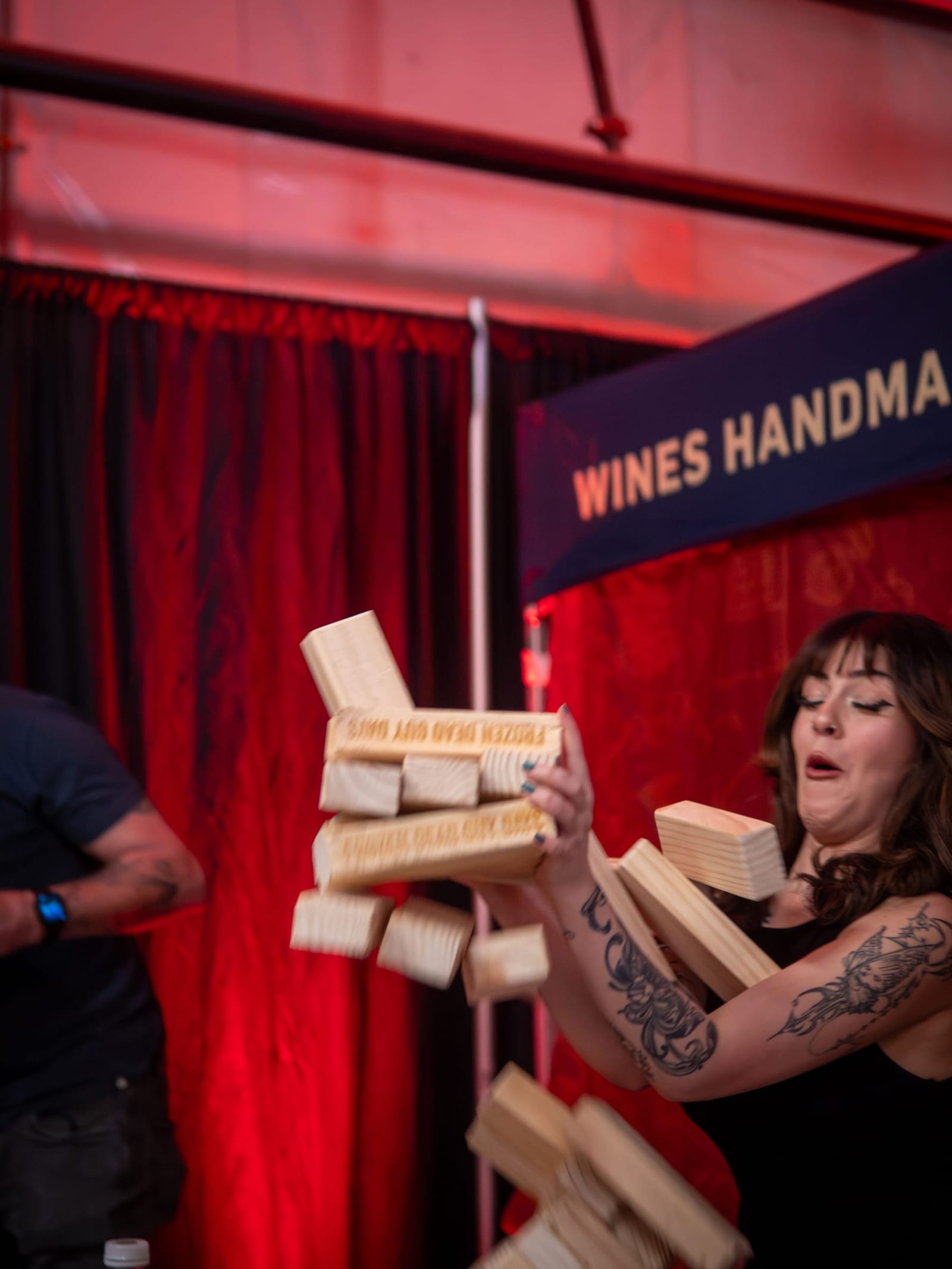 A giant wooden Jenga tower collapses mid-air as a woman flinches in surprise.