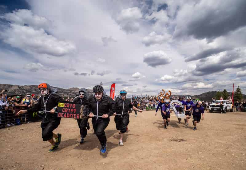 A team in black jumpsuits and pale corpse makeup races a "Cryo Crypt Deadites" coffin under cloudy skies.