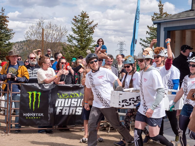 A coffin team in tire-track T-shirts walks past cheering spectators and a Monster Energy banner.