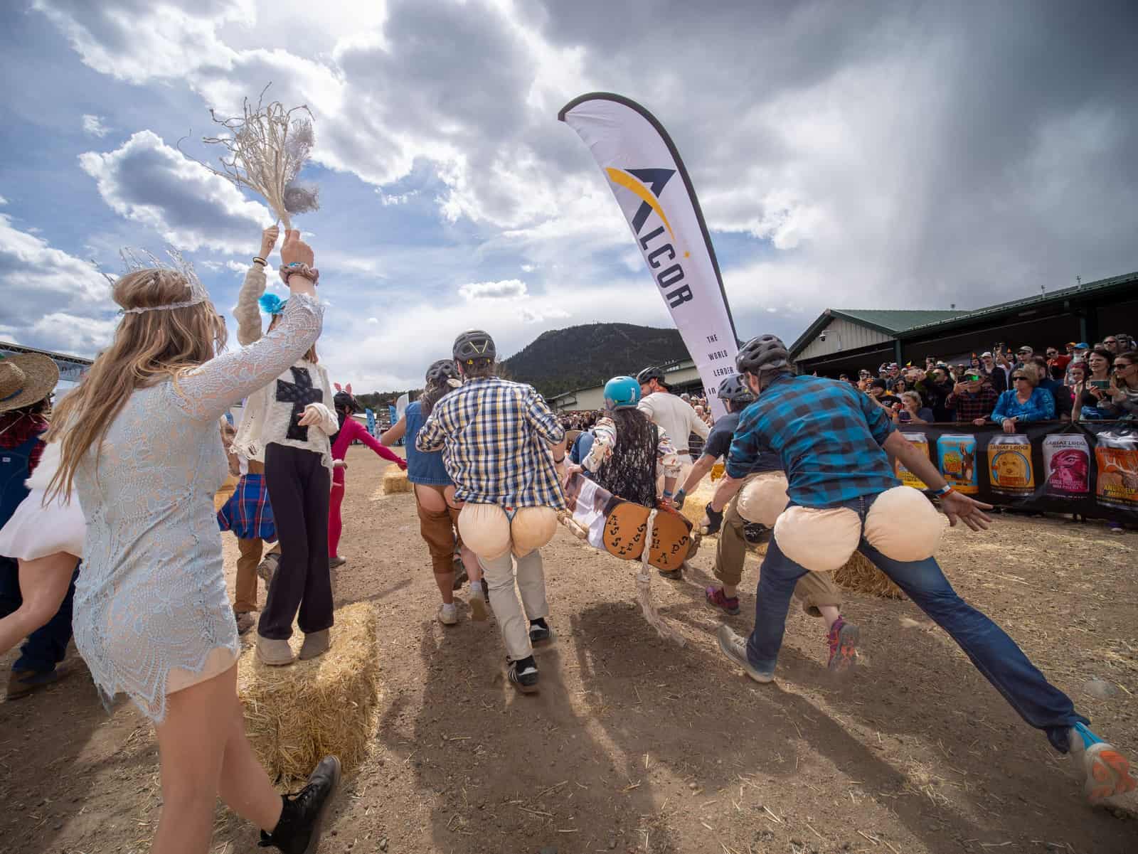 Seen from behind, a coffin team wearing oversized fake-bottom pads over their pants charges toward a packed grandstand under storm clouds.
