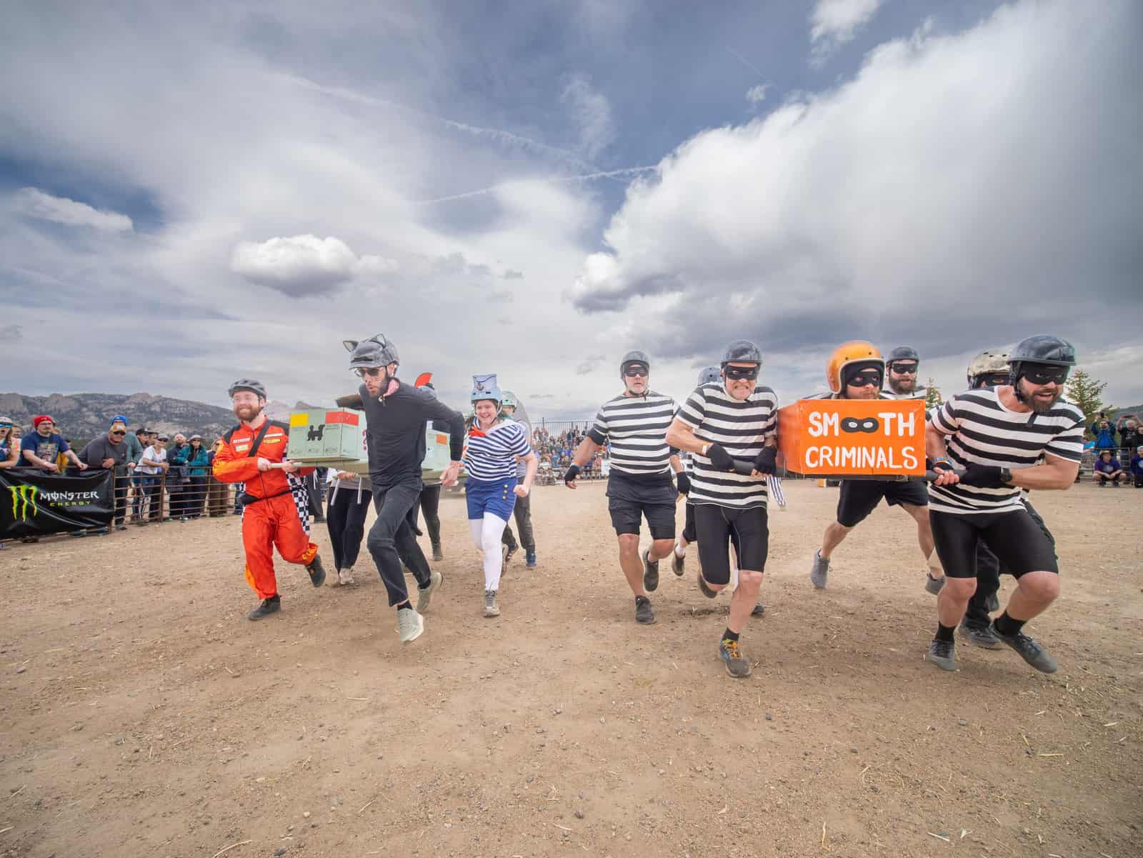 Racers in black-and-white convict stripes and eye masks run with an orange "Smooth Criminals" coffin.