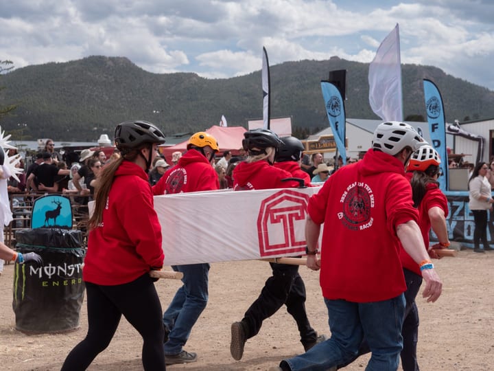 The Tuff Shed team in red hoodies races a white coffin with the Tuff Shed logo past a Monster Energy barrel.