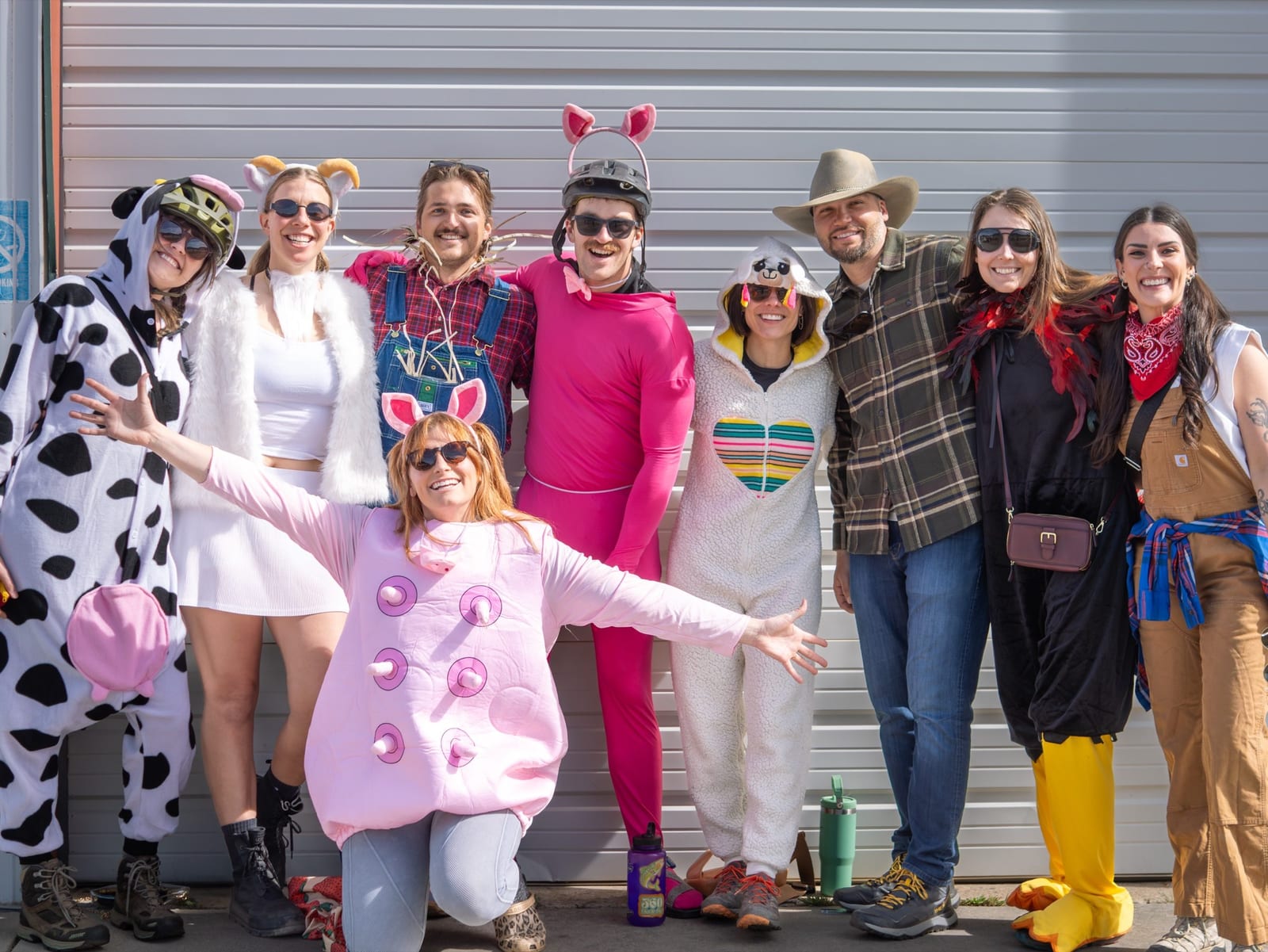 A coffin team in a cow onesie, a pink bunny suit and a rainbow onesie poses arms out at check-in.