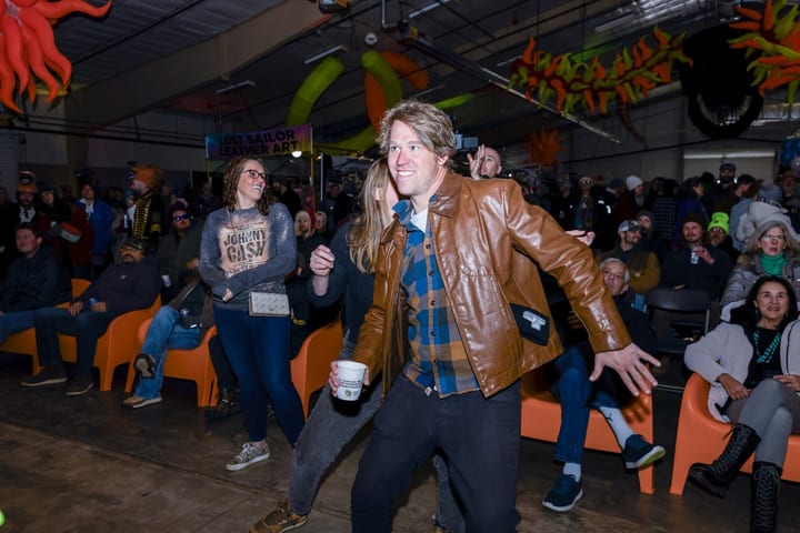 A man in a leather jacket dances mid-move in the Fire room.