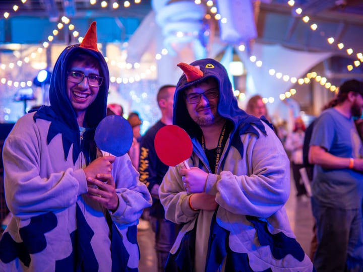 Two fans in pigeon onesies hold up ping-pong paddles.