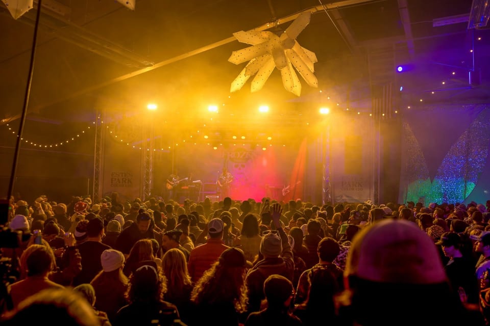 A huge crowd faces a stage glowing gold and red through haze, an inflatable ice crystal hanging overhead.