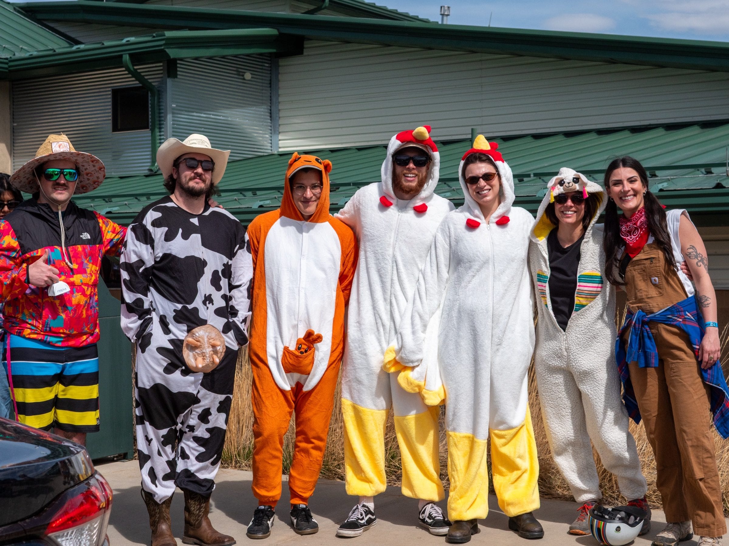 Friends in cow, chicken and tiger onesies grin at the camera outside the hall.