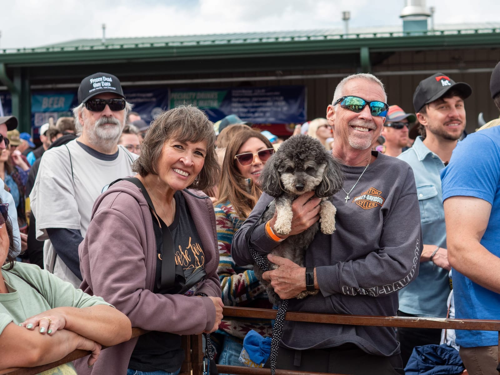 A smiling couple at the race rail, the man holding a fluffy gray poodle.