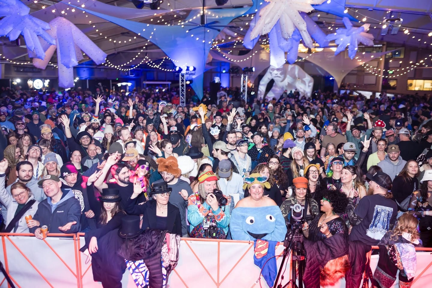 From the stage: a packed, costumed crowd cheers at the rail under giant inflatable ice crystals and string lights.