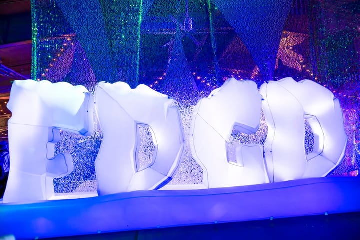 Giant glowing white letters spell FDGD in front of a sparkling blue wall.