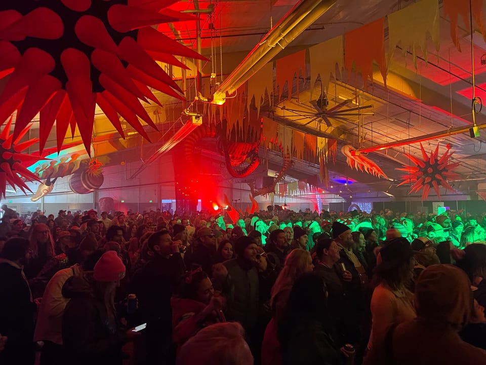 Huge red spiky inflatables hang over a packed crowd in green light in the Fire hall.
