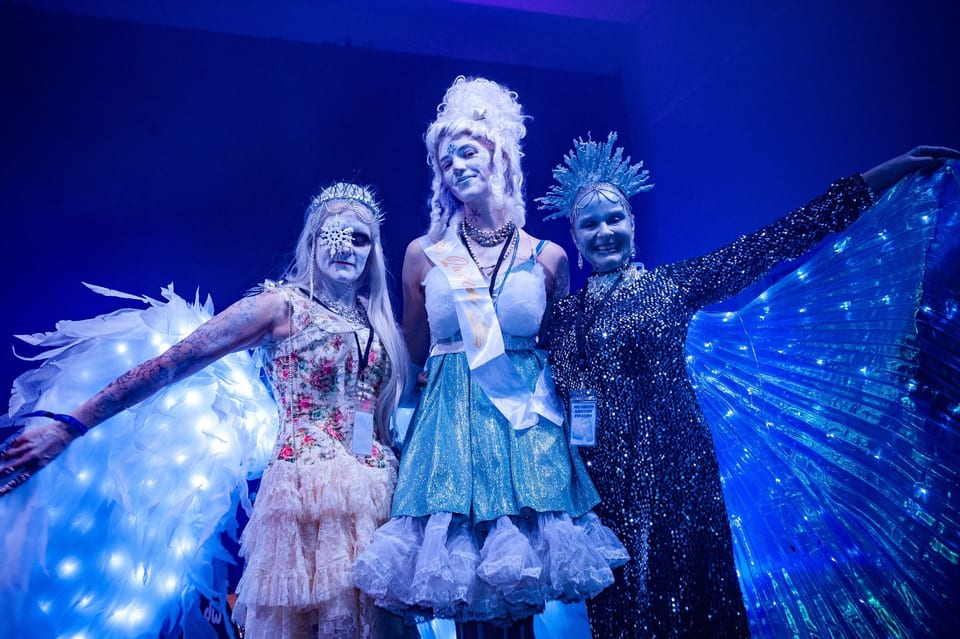 Three Ice Queen Contest finalists in frosted make-up, a sash and glowing wings on stage.
