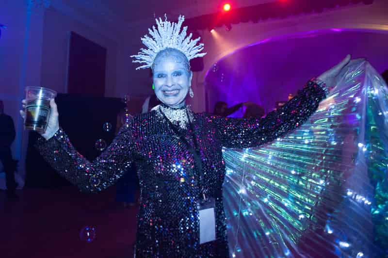 A beaming Ice Queen in frosted blue face paint, an icicle crown and glowing wings at The Frozen Blue Ball.