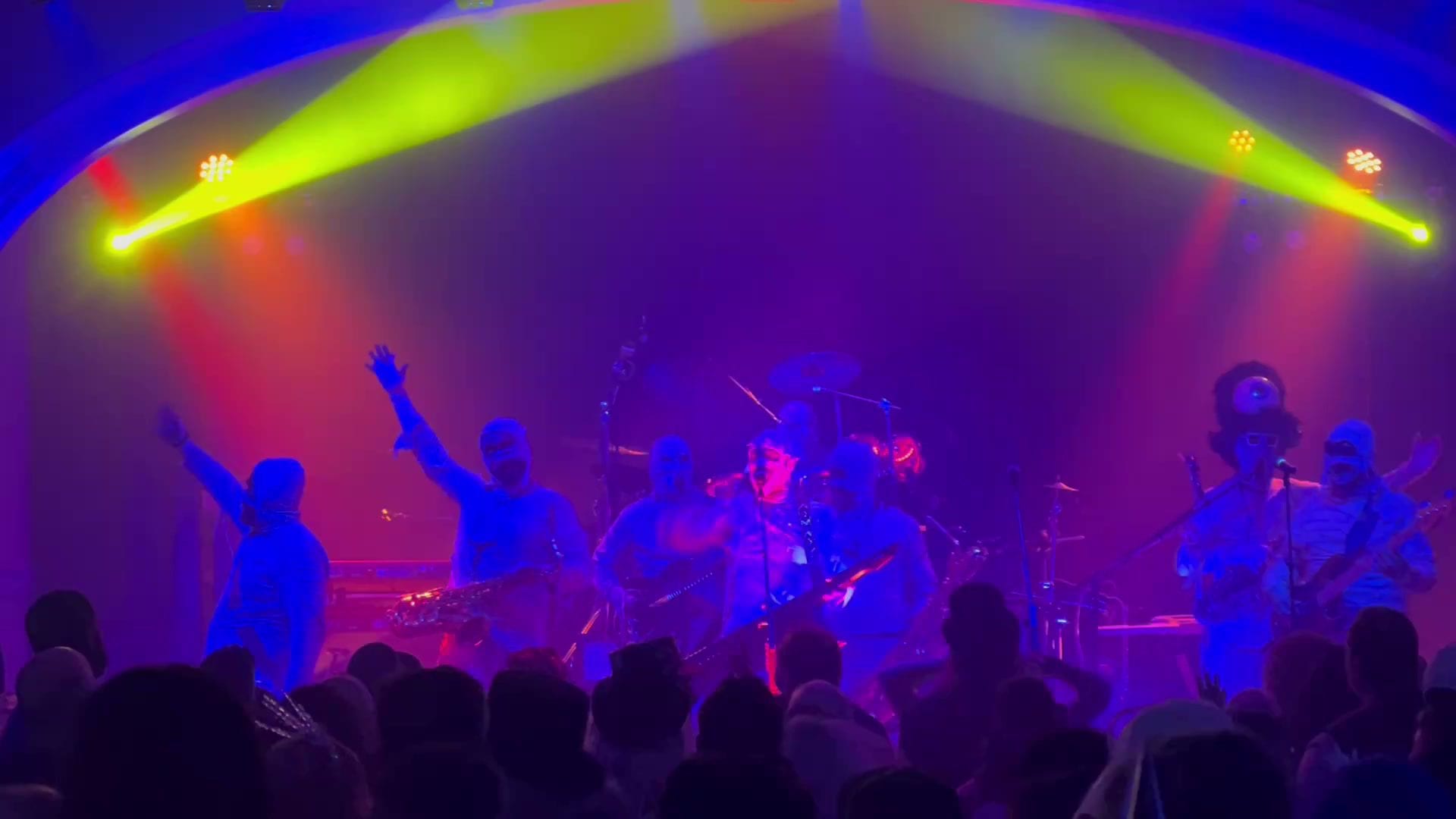 Here Come The Mummies, in mummy wraps, raise their arms under yellow and red beams at The Frozen Blue Ball.