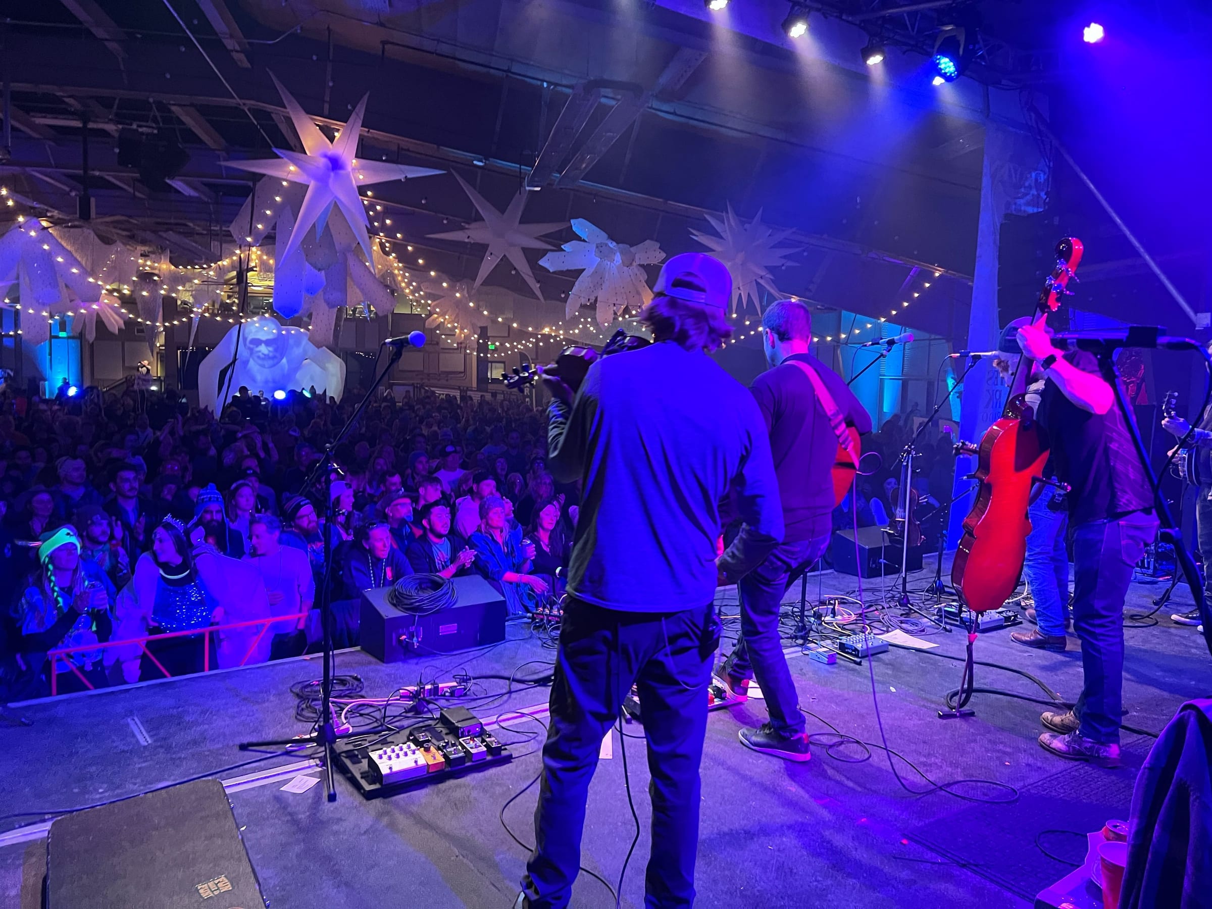 View from behind a string band toward a packed indoor crowd under snowflake inflatables and string lights.