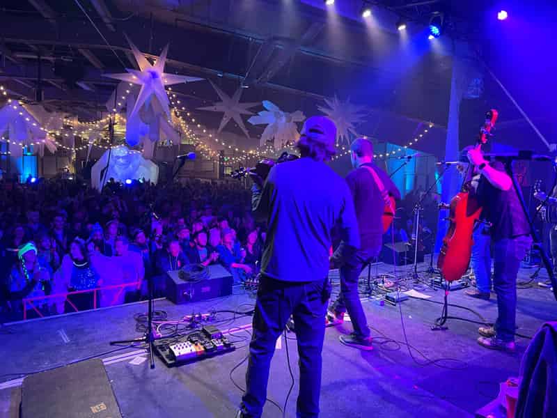 View from behind a string band toward a packed indoor crowd under snowflake inflatables and string lights.