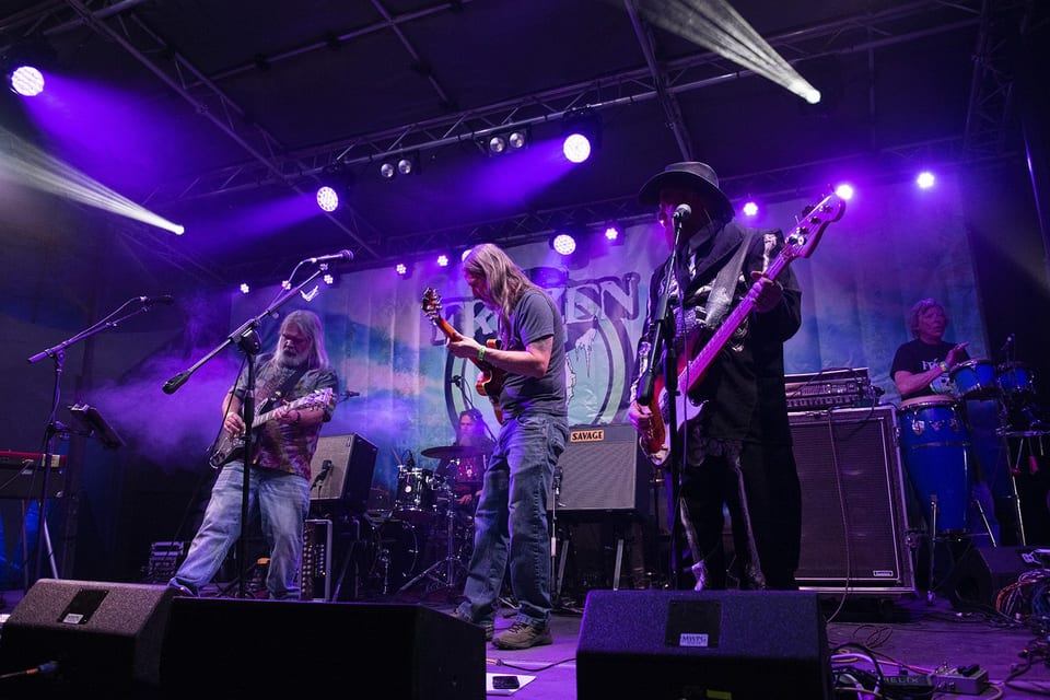 A four-piece band plays under purple beams.