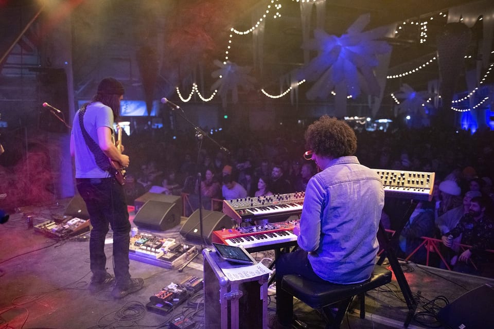 From behind a guitarist and a keyboardist toward the crowd under string lights.