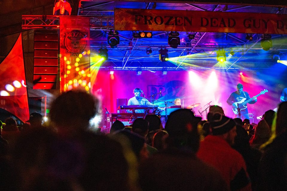 Lasers and beams sweep under the Frozen Dead Guy Days banner as the band plays, the crowd in silhouette.