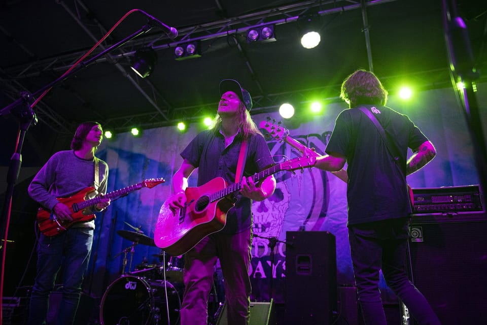 Three guitarists play under green and purple lights.