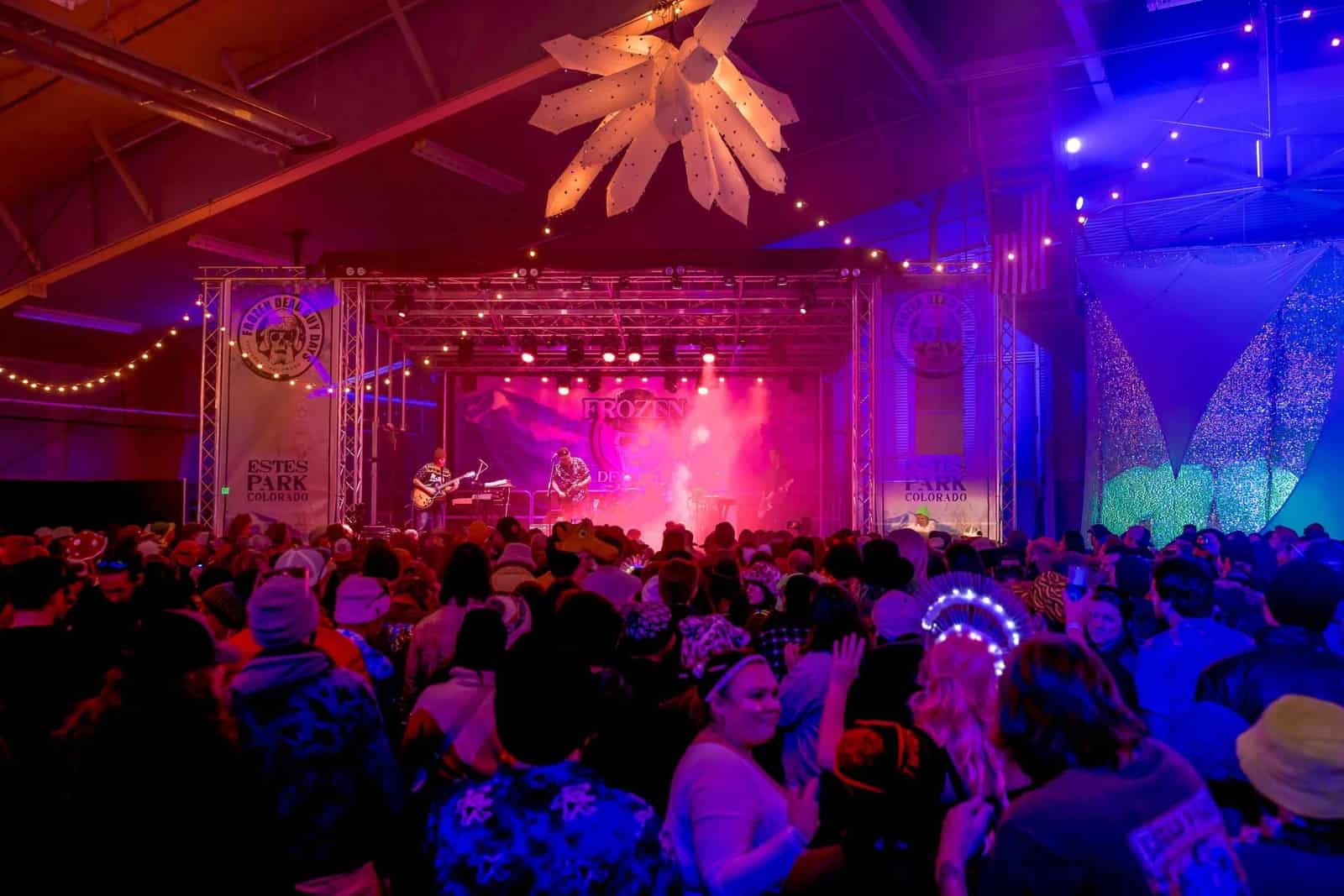 The Ice stage glows pink through haze over a packed crowd, one fan in an LED headdress.