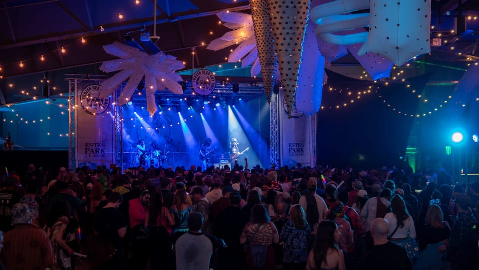 A band plays under blue beams on the Ice Room stage before a packed crowd, giant ice crystals overhead.