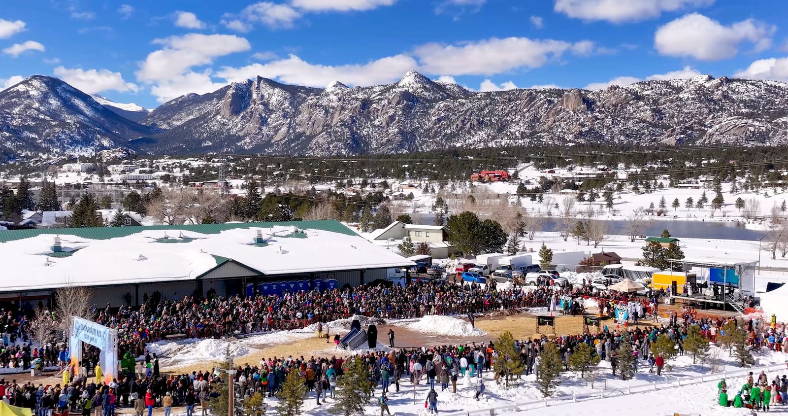 Aerial view of snow-capped peaks towering over a packed, snowy coffin course and the Events Complex.